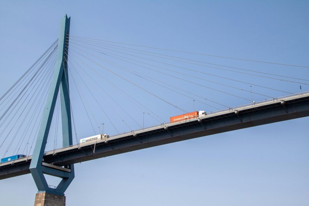 pexels-photo-12903692-12903692 Trucks crossing the Köhlbrand Bridge in Hamburg, Germany, under a clear blue sky.