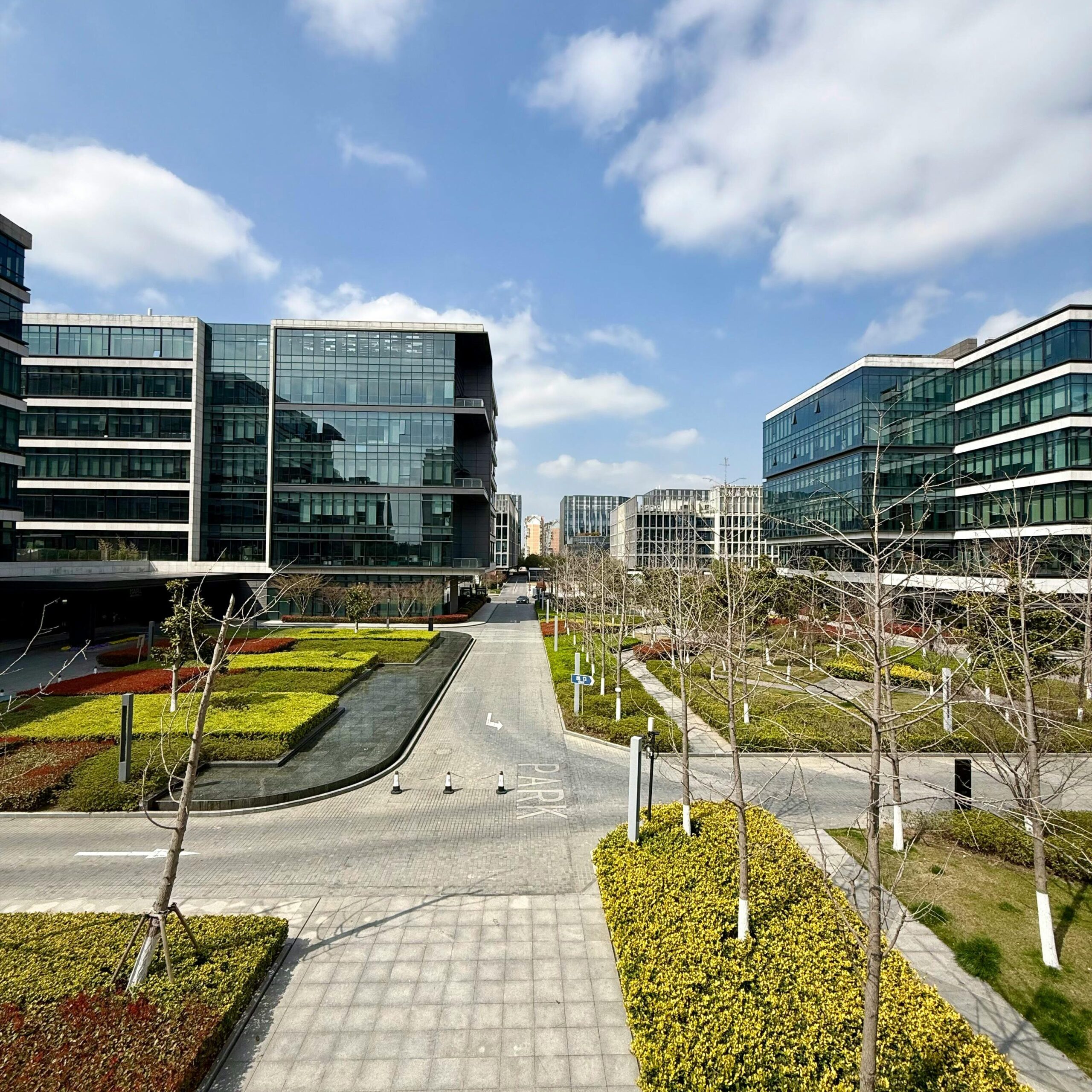 Sunny day view of a modern business park featuring glass buildings, pathways, and landscaped gardens.